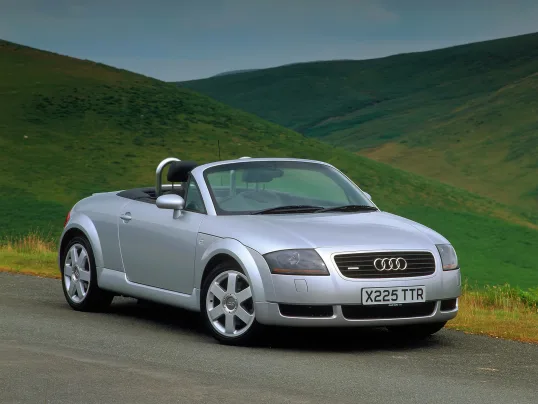 Audi TT Roadster prata parado de frente com montanhas ao fundo