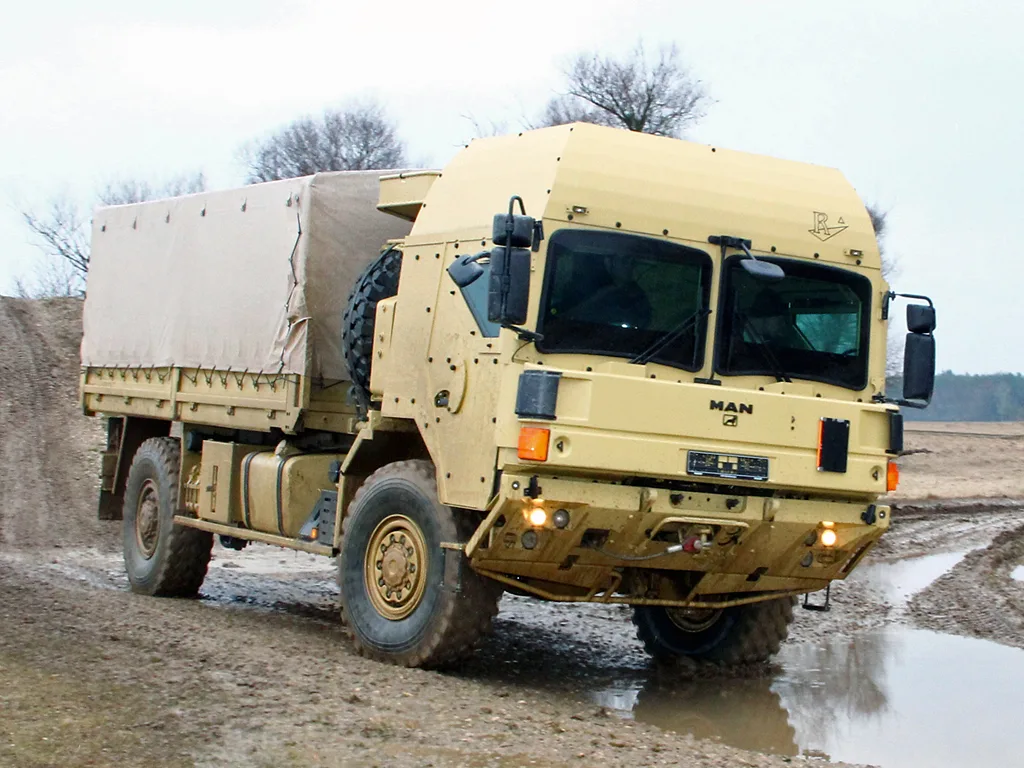 Caminhão MAN HX 18.330 BB 4x4 bege, visto de frente e com faróis acesos