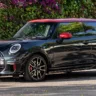 Mini John Cooper Works hatch preto com detalhes vermelhos, visto de lado e com flores ao fundo