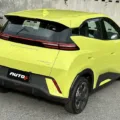 BYD Dolphin Mini amarelo parado de traseira em frente a um portão branco com árvores ao fundo