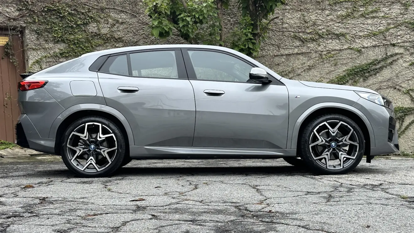 BMW iX2 cinza parado de lateral com muro de cimento ao fundo