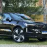 Volvo EX90 Ultra preto parado de frente com muro amarelo e árvores ao fundo