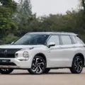 Novo Mitsubishi Outlander PHEV branco parado de frente com árvores ao fundo