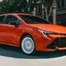 Toyota Corolla hatch FX Edition 2026 laranja com detalhes pretos, visto de lado e com faróis acesos