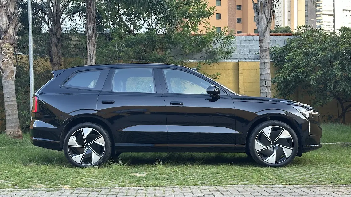 Volvo EX90 Ultra preto parado de lateral com muro amarelo e árvores ao fundo