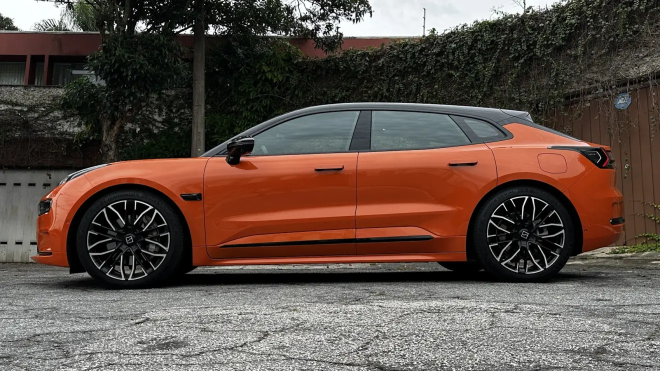 Zeekr 001 laranja parado de lateral com muro e plantas ao fundo