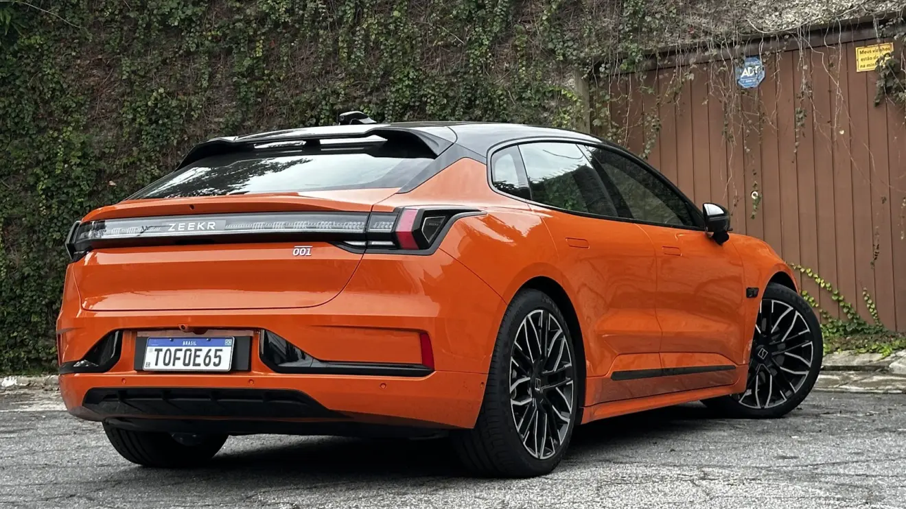 Zeekr 001 laranja parado de traseira com muro e plantas ao fundo