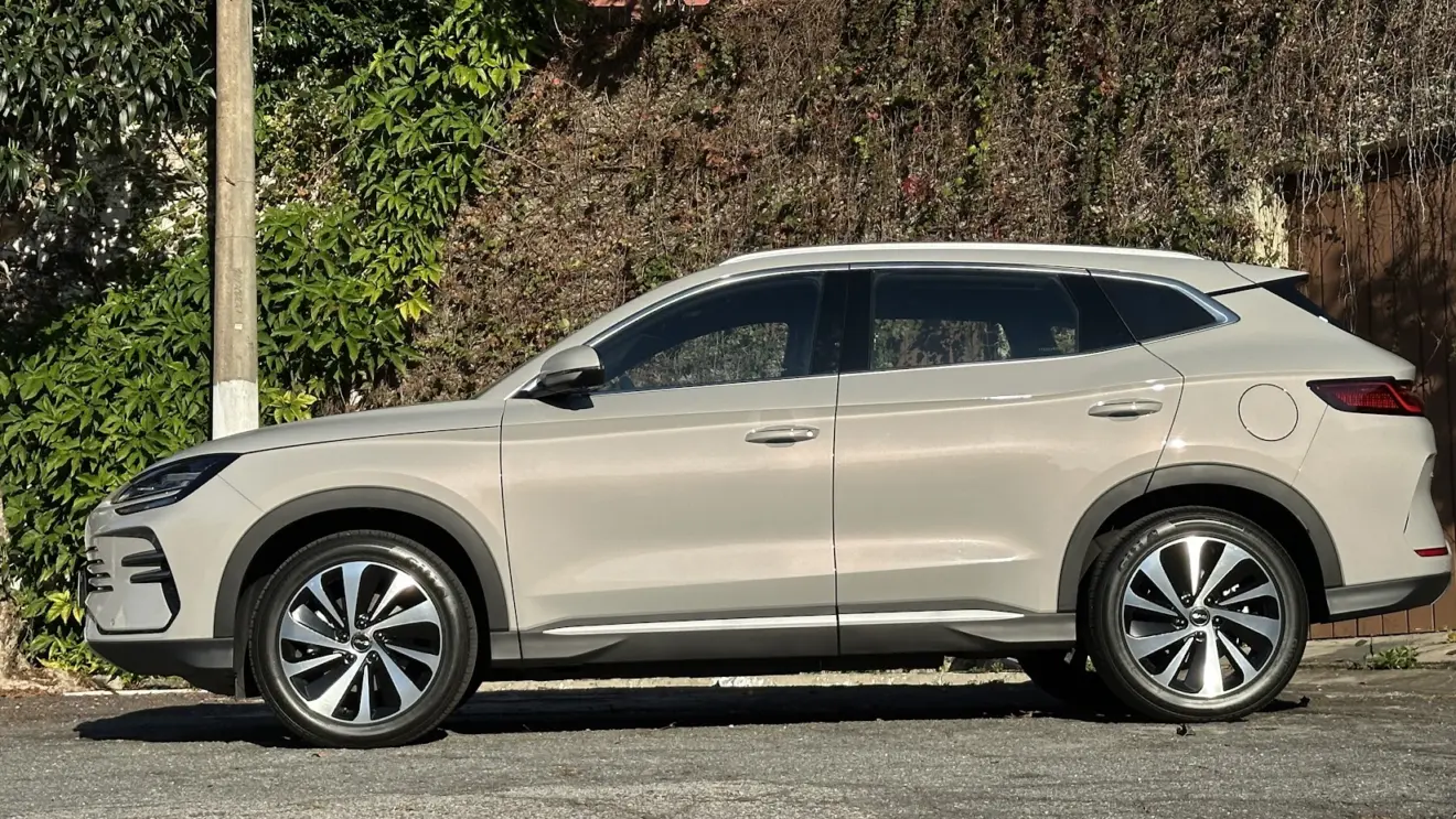 BYD Song Plus dourado parado de lateral com muro e plantas ao fundo