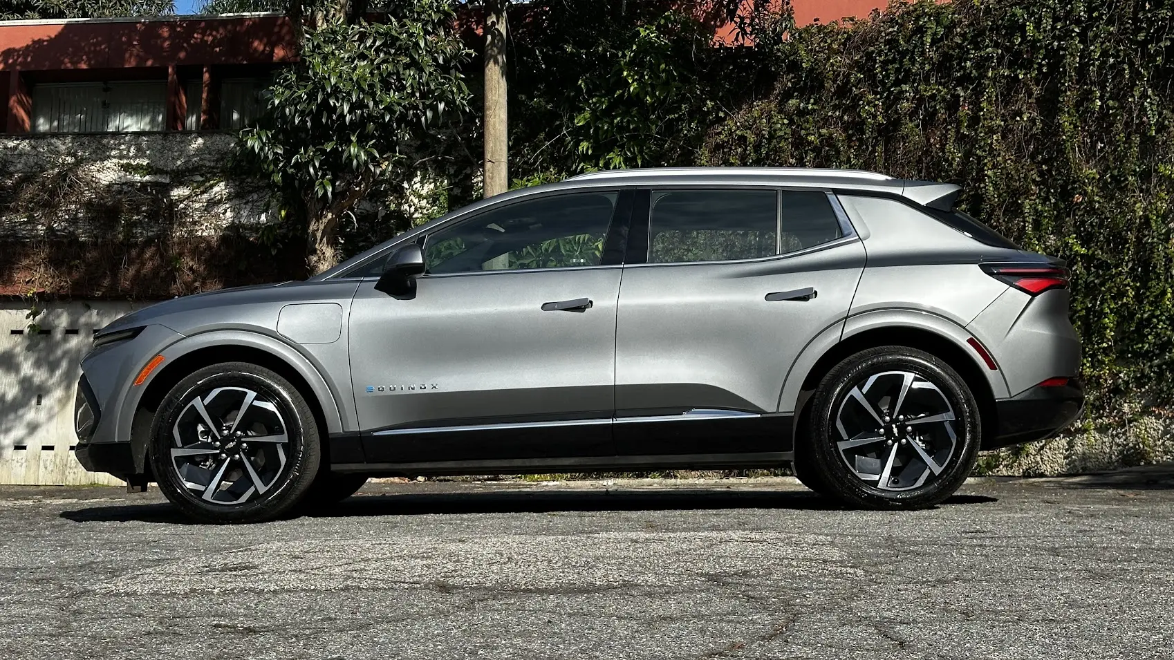 Chevrolet Equinox EV AWD prata parado de lateral com muro e plantas ao fundo