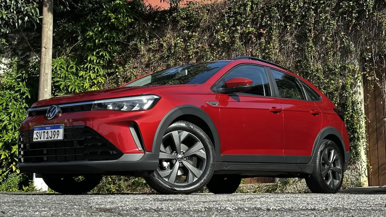 Volkswagen Nivus Comfortline 200TSI vermelho parado de frente/lateral com muro e plantas ao fundo