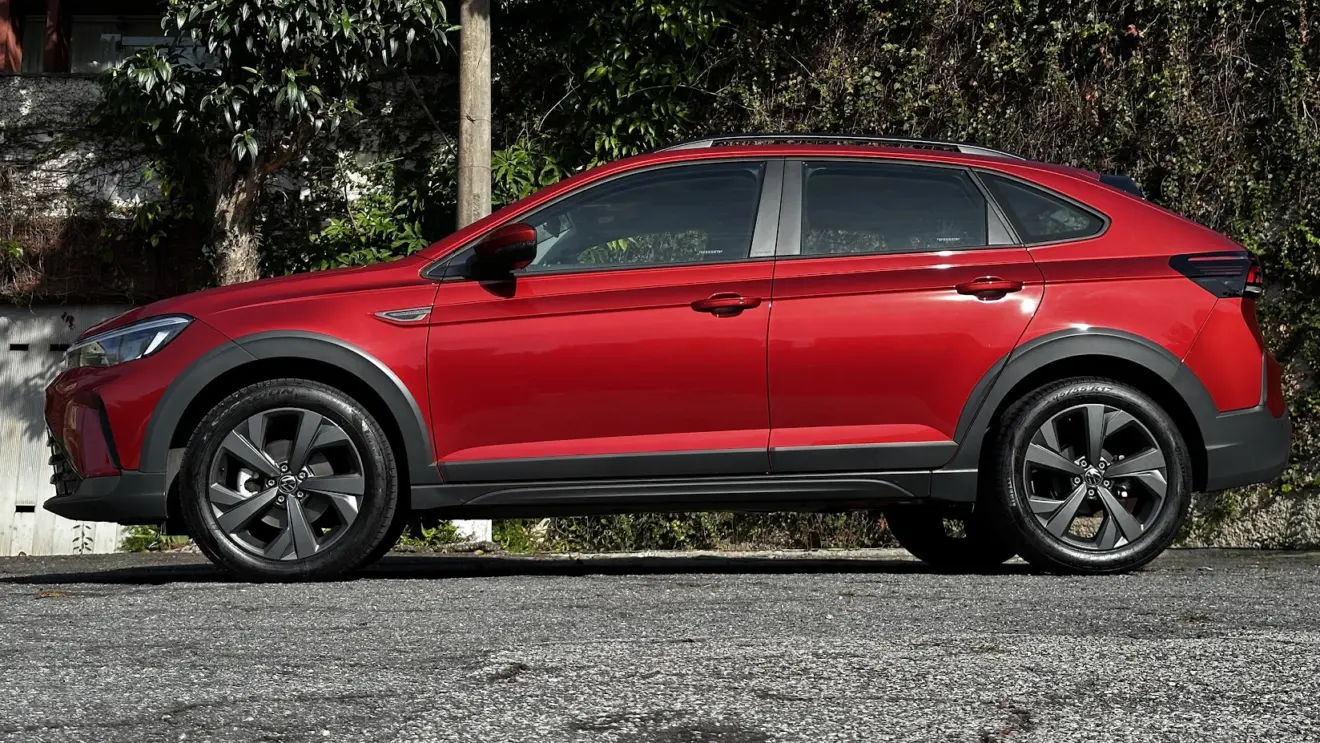 Volkswagen Nivus Comfortline 200TSI vermelho parado de lateral com muro e plantas ao fundo