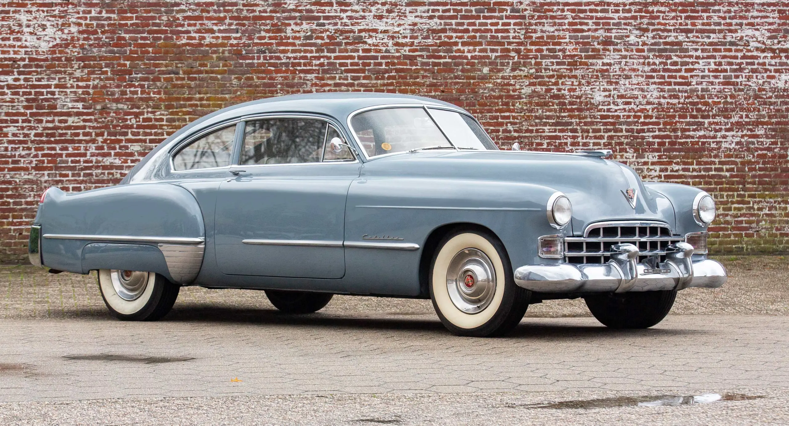 Cadillac Série 62 1948 azul parado de lateral com muro de tijolos ao fundo