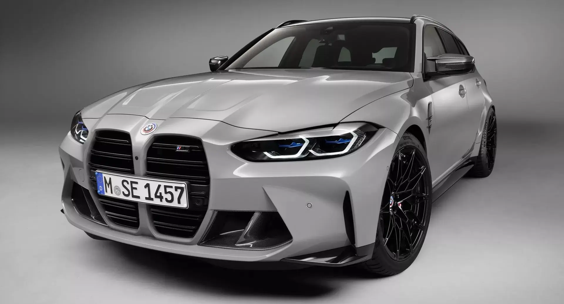 BMW M3 Touring prata parada de frente com fundo neutro