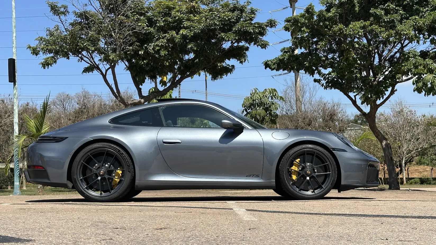 Porsche 911 Carrera GTS cinza parado de traseira com árvores ao fundo