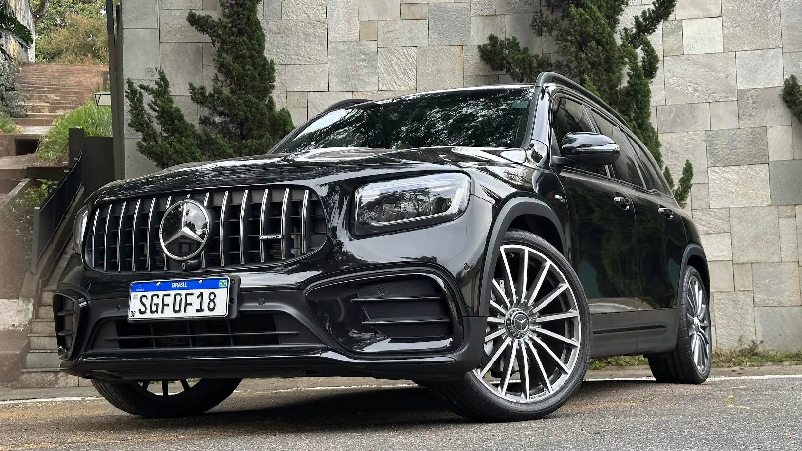 Mercedes-AMG GLB 35 4Matic preto parado de frente com muro de pedras e árvores ao fundo