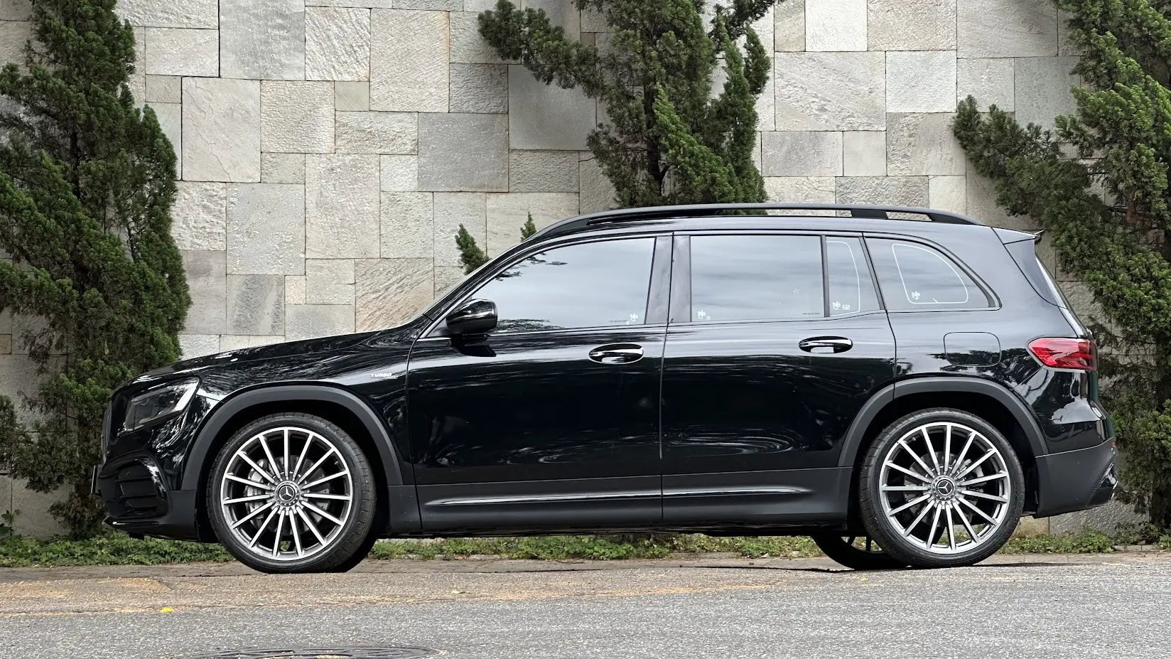Mercedes-AMG GLB 35 4Matic preto parado de lateral com muro de pedras e árvores ao fundo