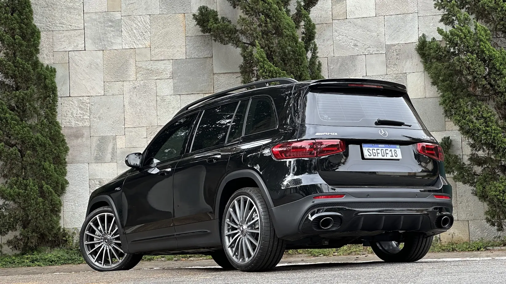 Mercedes-AMG GLB 35 4Matic preto parado de traseira com muro de pedras e árvores ao fundo
